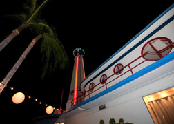 A nighttime view of the Crossroads tower, globe and ocean liner building framed by palm trees. Photo courtesy of Martha Adams, 2009.